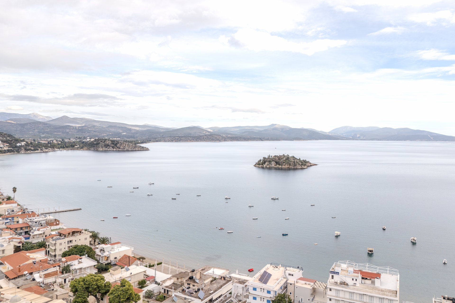 A scenic view of the beautiful bay and sandy beach of Tolo, Greece, with clear blue water.